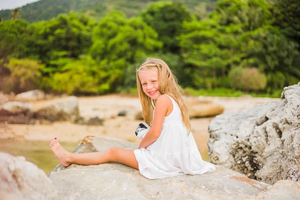 Chica alegre con el pelo largo en un vestido blanco sentado en una roca junto al mar — Foto de Stock