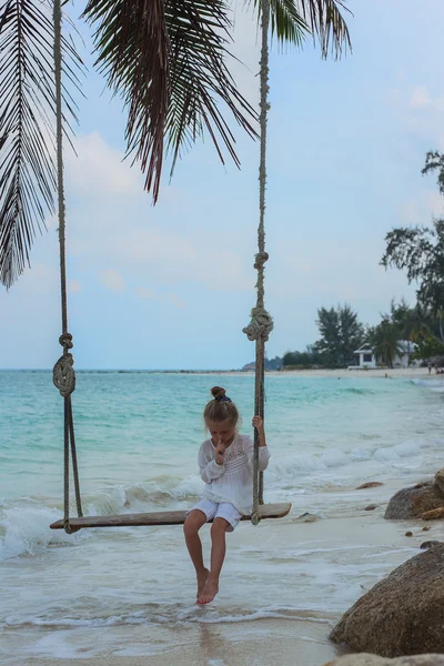 Temprano en la mañana la chica en vestido blanco balanceándose en el columpio en la playa profundo en el pensamiento — Foto de Stock