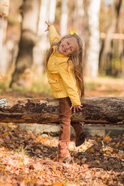 Neşeli küçük kız bir kırık ağaç gövdesi sonbahar ormandaki oturur