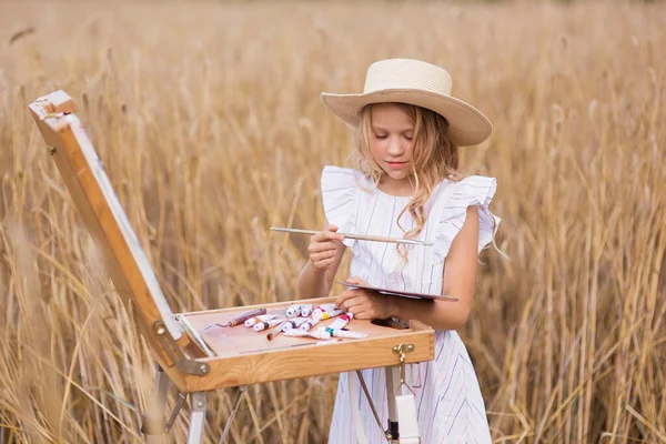 かわいい女の子は小麦畑の絵を描く — ストック写真
