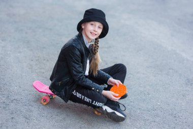 Genç bir kız sokakta kaykayın üzerinde oturur ve çocuklar arasında popüler olan yeni bir oyuncak çalar ve onların konsantre olmalarına yardımcı olur. Bir çocuk Pop It Fidget oyuncağıyla oynuyor. Stres önleyici oyuncak