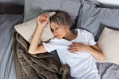 Orta yaşlı bir kadın evde yatakta uyuyor.