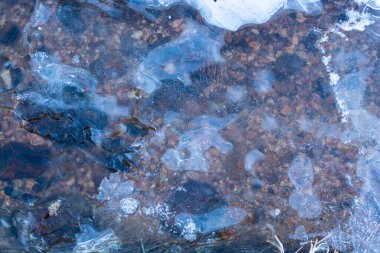 Hava kabarcıkları ve süslü fay hatları olan buzlar, karla kaplı yerler, soyut desenler, arka plan. Altında koyu su akan mavi buz dokusu. Kış ormanındaki bir gölde donmuş su