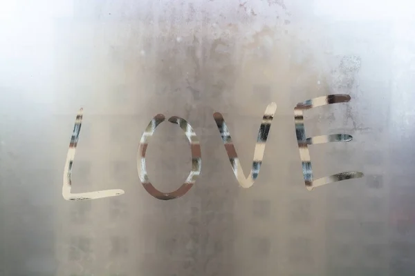 Love drawn on misted window on the background of the city. Inscription love with finger on misted glass. Hand Drawn love on window.