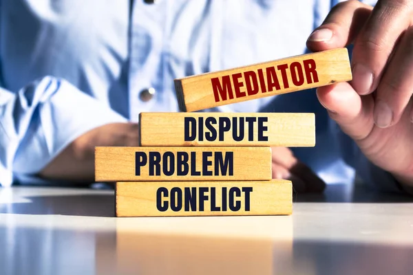 Bir adam kelime Arabulucu, anlaşmazlık, sorun, çatışma ile ahşap bloklar tutar. Uyuşmazlıkların arabulucu tarafından çözülmesi. Uyuşmazlık Çözümü ve Arabuluculuk. Üçüncü taraf, aracı.