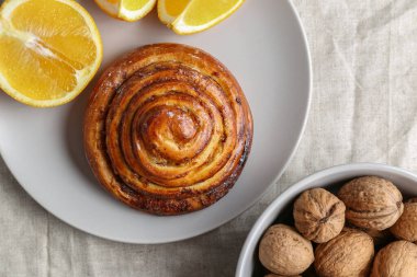 Tarçın gri bir tabakta yuvarlanır parlak bir masada ceviz ve portakal dolu bir tabakla.