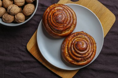 Tarçınlı çörekler gri bir tabakta, karanlık bir masada, cevizli.
