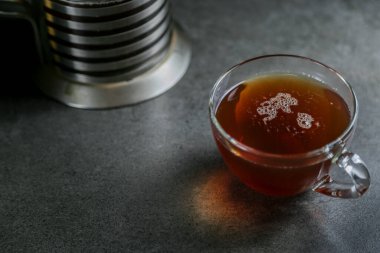 Cam bardakta bir fincan sıcak siyah çay ve gri seramik tezgahta bir çaydanlık..