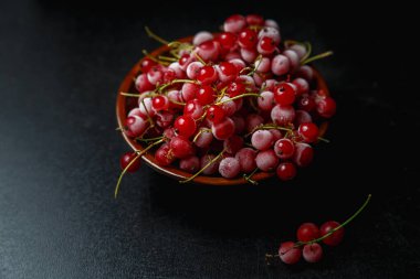 Kahverengi bir seramik vazoda siyah arka planda donmuş kırmızı üzümler. Yakın plan. Doğal ve sağlıklı vitamin açısından zengin donmuş dut..