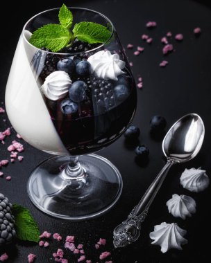 Siyah arka planda gözlüklü Blackberry panna cotta. Geleneksel İtalyan tatlısıyla böğürtlen reçeli ve nane yaprağı.