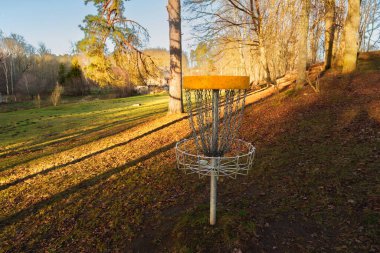 Sıcak günbatımı ışığı ve uzun gölgeleri olan manzaralı bir parkta duran golf sepeti. Doğal bir manzarada açık hava sporları ve eğlence kavramı.