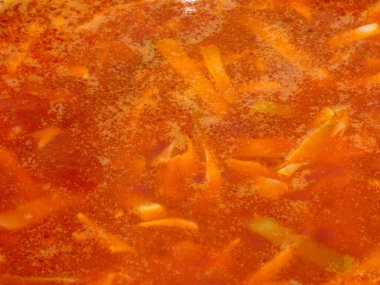 Kesilmiş sebze ve köpükle yoğun portakal kırmızısı kaynar su çorbası..