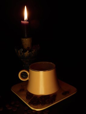 Sarı espresso fincanı, kahve çekirdekleri ve yanan mumla dramatik bir hayat..