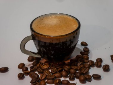 Temiz beyaz bir masada tek kahve çekirdeği olan zarif gri cam bardak..