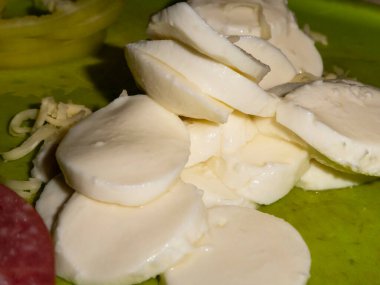 Parlak yeşil bir kesme tahtasında beyaz mozzarella peyniri dilimleri..
