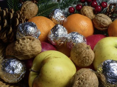 Taze portakallar, elmalar, cevizler ve gümüş sarısı şekerlemelerden oluşan şenlikli bir yakın plan..