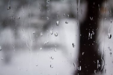 Pencere camındaki su damlacıklarının soyut arkaplanı ve dışarıda bulanık ağaçlar.