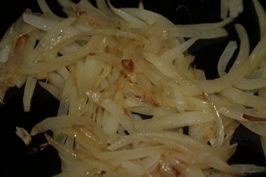 Altın soğan dilimlerinin yakın planda koyu bir tavada yağda sotelenmesi..