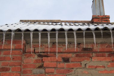 Kış sahnesinde buz saçakları tuğla bir binanın çatısında. Soğuk hava, mevsimsel değişiklikler ve ev bakımı kavramı.