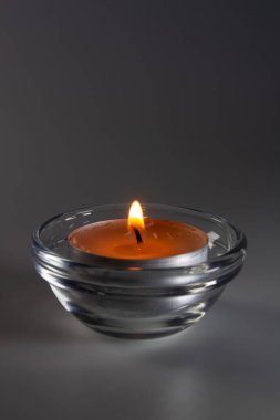 Arka planda cam bir kasede yanan küçük bir mum.