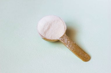 White collagen protein powder on a measuring spoon and scattered over the background clipart