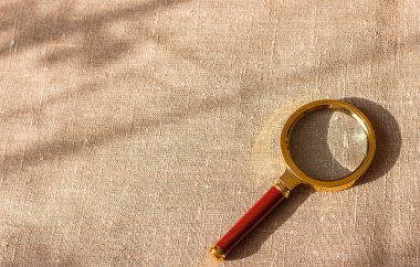 Tekstil tuvalinin arka planında güneş parıldayan klasik büyüteç.