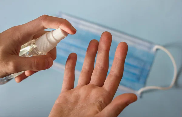 cleansing and disinfecting hands with an antiseptic spray, a bottle of sanitizer in hands against the background of a medical mask, hygiene during quarantine and coronavirus pandemic