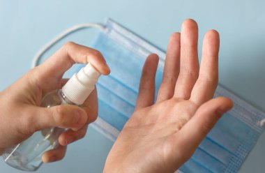 El temizleme ve antiseptik sprey ile dezenfekte etme, tıbbi maskenin arka planına karşı bir şişe dezenfekte etme, karantina ve koronavirüs salgını sırasında hijyen.