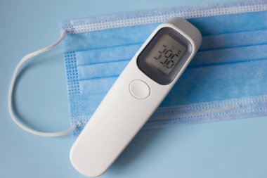 Tıbbi bir maskenin arka planında yüksek sıcaklık ve ısı göstergeleriyle elektronik temas olmayan termometre