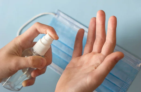 cleansing and disinfecting hands with an antiseptic spray, a bottle of sanitizer in hands against the background of a medical mask, hygiene during quarantine and coronavirus pandemic