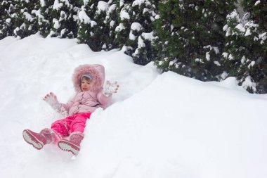 Pembe kışlık elbiseli küçük bir kız karla kaplı bir şehir sokağında yüzünde neşeli duygularla mutlu bir çocukluk ve aktif bir kış yaşam tarzıyla duruyor.