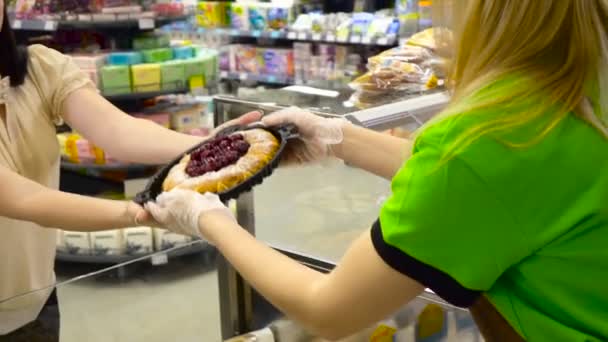 Працівник хлібопекарні продає торти, передаючи їх клієнту через лічильник — стокове відео