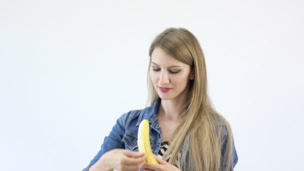 Όμορφο κορίτσι τρώει μια μπανάνα σε λευκό φόντο qHD + 4k — Αρχείο Βίντεο