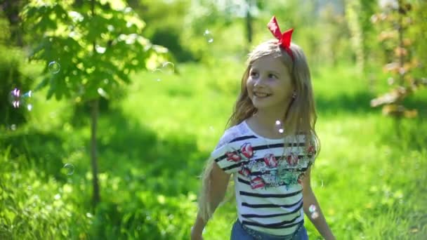 Menina pegando bolhas de sabão na luz solar. Criança feliz a rir. Inflação da lente — Vídeo de Stock