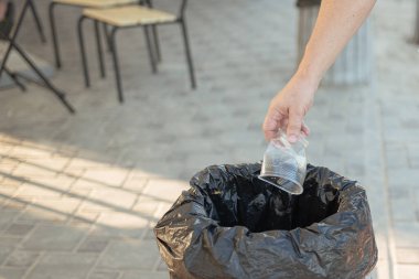 Bir adamın eli, plaj kafe bölgesindeki plastik için boş bir plastik bardağı çöp kutusuna atar.