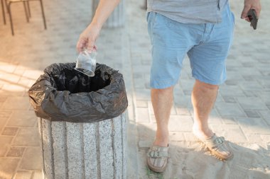 Bir adamın eli, plaj kafe bölgesindeki plastik için boş bir plastik bardağı çöp kutusuna atar.