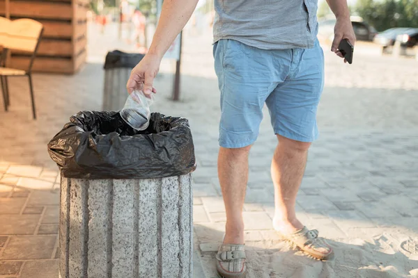A man\'s hand throws an empty plastic cup into a waste bin for plastic on the territory of a beach cafe