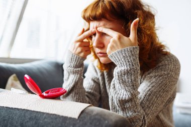 Genç bir kadın aynadaki sorunlu yüz derisine, tatminsiz yüz ifadesine, ergenlik sorununa bakar.