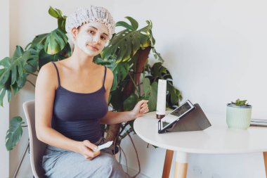 Genç bir kadın evdeki sandalyede otururken nemlendirici kozmetik maske takıyor, blog yazarı, internet üzerinden canlı yayın yapıyor.