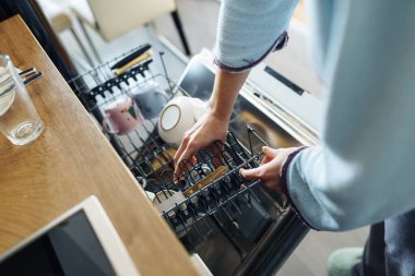 Bulaşık makinesine kirli bulaşık koyan genç bir kadın. Mutfakta ev işi.
