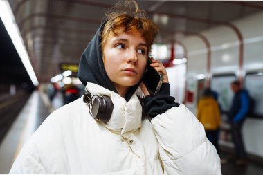 Yeraltı toplu taşımacılığındaki kışlık ceketli genç kadın cep telefonu kullanıyor