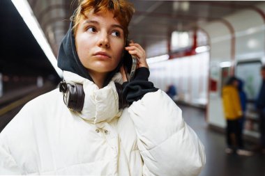 Yeraltı toplu taşımacılığındaki kışlık ceketli genç kadın cep telefonu kullanıyor