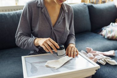 Kadın evde kıyafetlerle ilgileniyor, aletle ipliği kesiyor, eşyaları sürekli kullanıyor, çevre dostu.