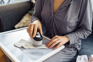 Kadın evde kıyafetlerle ilgileniyor, aletle ipliği kesiyor, eşyaları sürekli kullanıyor, çevre dostu.