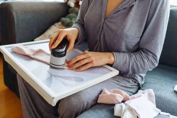 Kadın evde kıyafetlerle ilgileniyor, aletle ipliği kesiyor, eşyaları sürekli kullanıyor, çevre dostu.