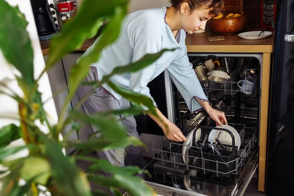 Bulaşık makinesine kirli bulaşık koyan genç bir kadın. Mutfakta ev işi.