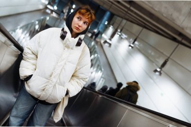 Metronun altındaki yürüyen merdivende sıcak beyaz ceketli genç bir kadın.