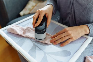 Kadın evde kıyafetlerle ilgileniyor, aletle ipliği kesiyor, eşyaları sürekli kullanıyor, çevre dostu.