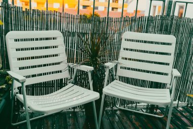 Bahçe beyazı plastik sandalyeler terasta, küçük balkon bahçesi batan güneş ışınlarıyla kaplı.
