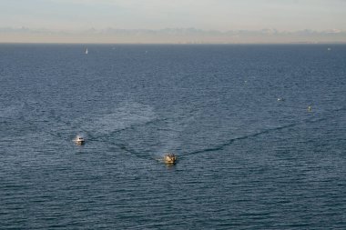 Adriyatik mavi denizi boyunca uzanan çok sayıda teknenin arka planında karla kaplı Alp dağları var..